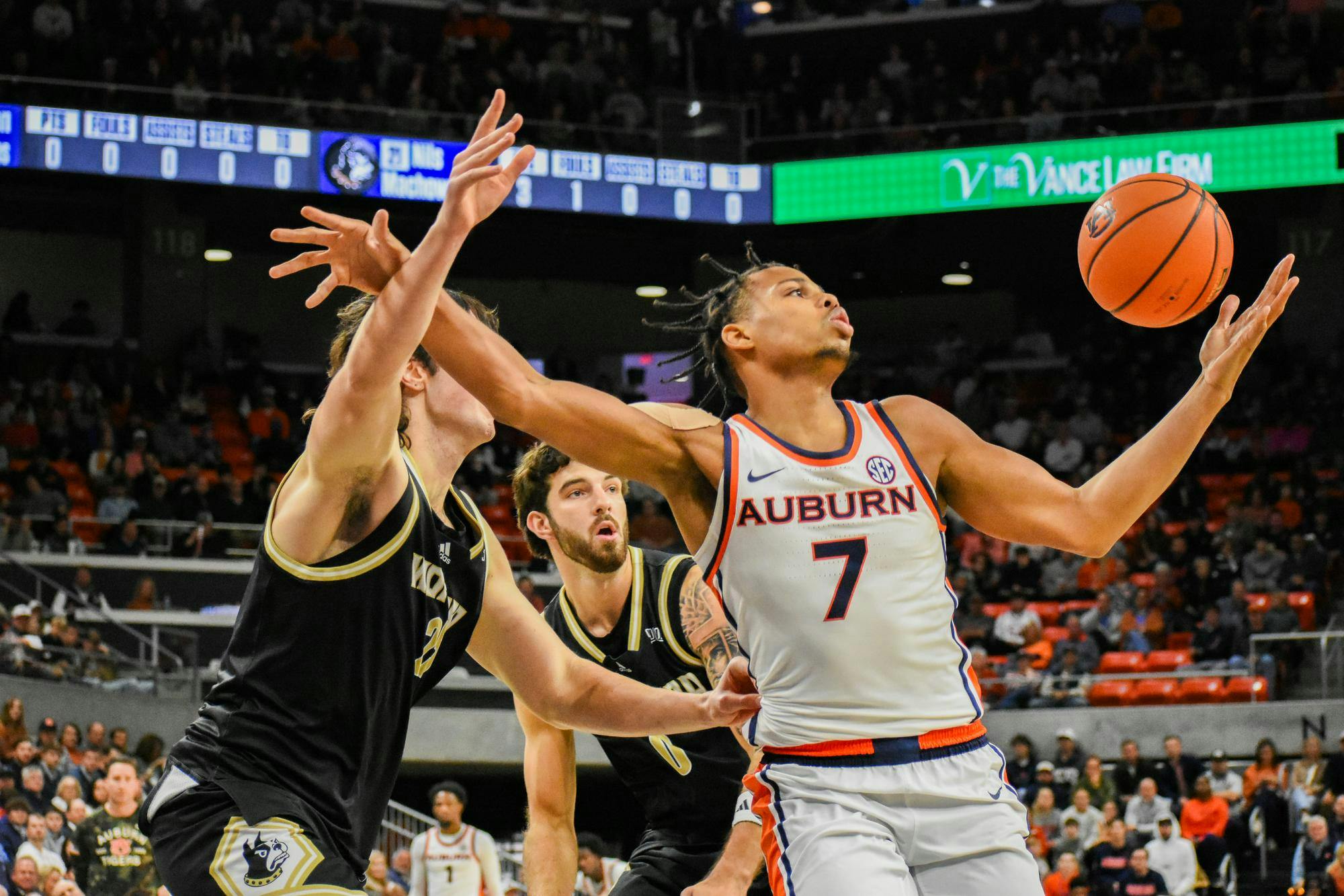 A player in an Auburn uniform reaches for a basketball while two opponents defend nearby, with a crowded arena in the background.
