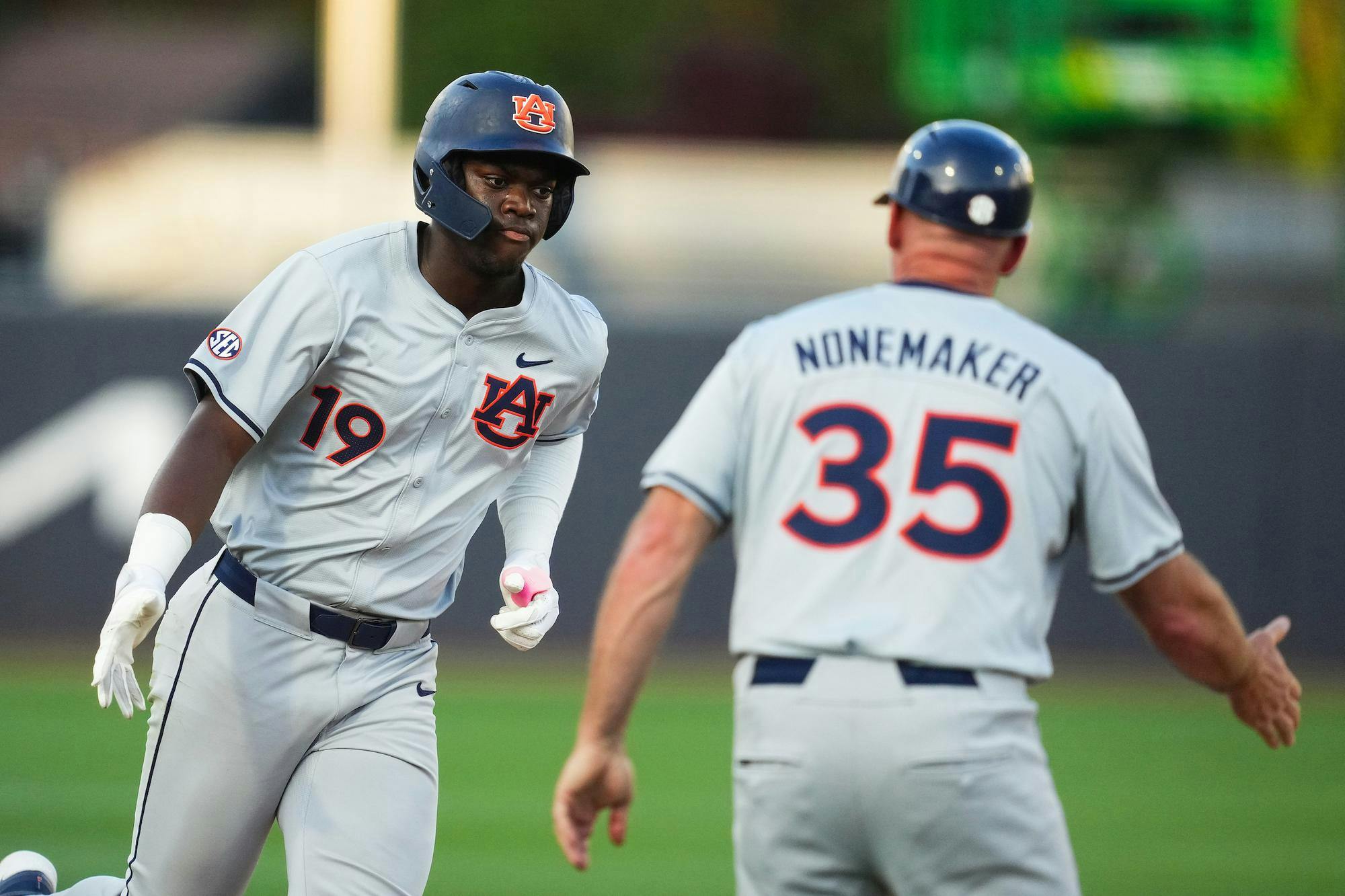 A baseball player in a gray uniform with the number 19 runs towards a coach wearing the number 35.