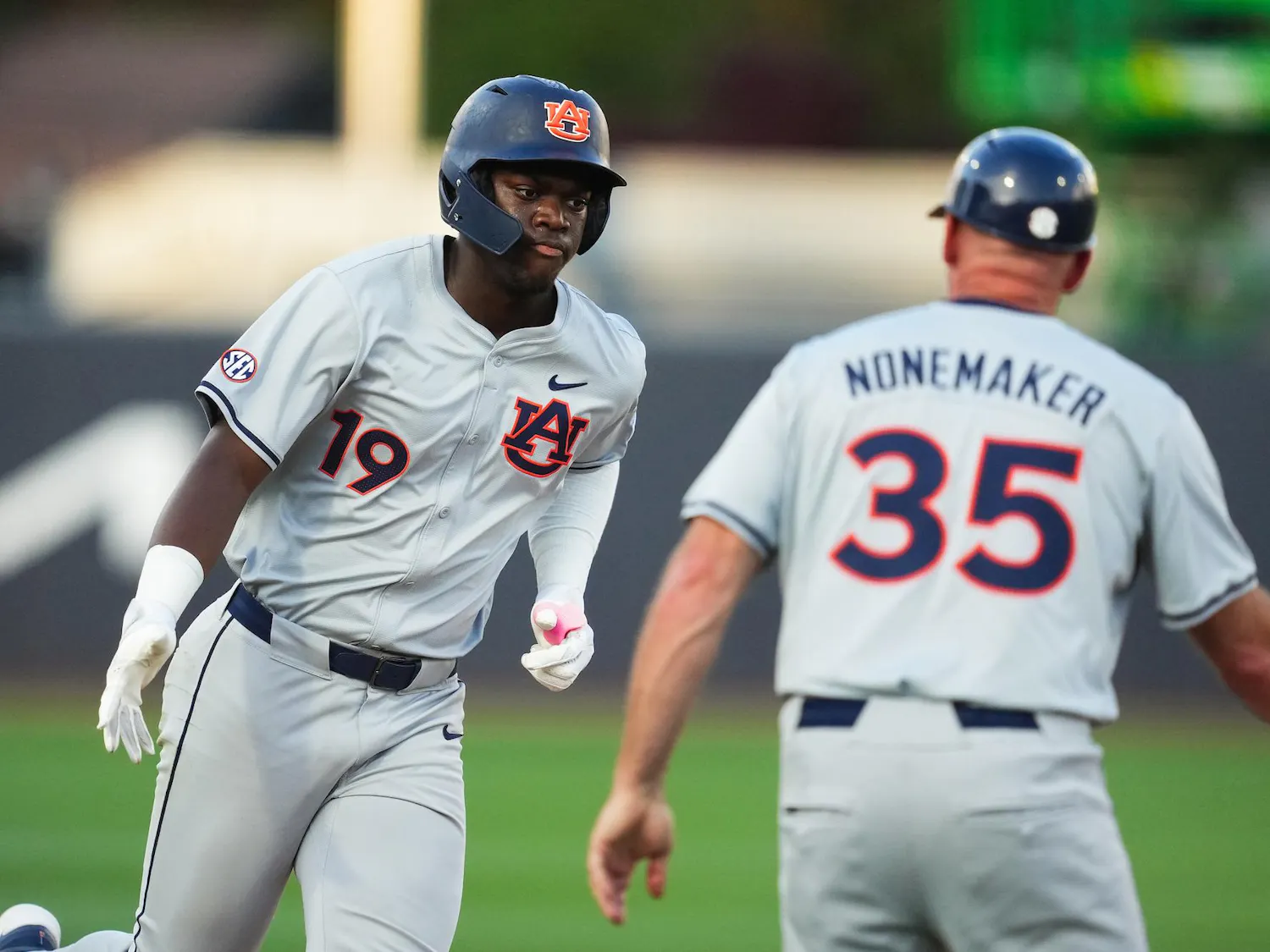 A baseball player in a gray uniform with the number 19 runs towards a coach wearing the number 35.