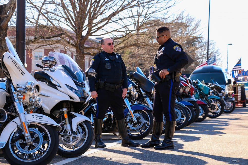 <p>Two officers with the Auburn Police Department chat in front of a row of motorcycles set to lead Auburn's Mardi Gras parade held on Feb. 18, 2023.</p>