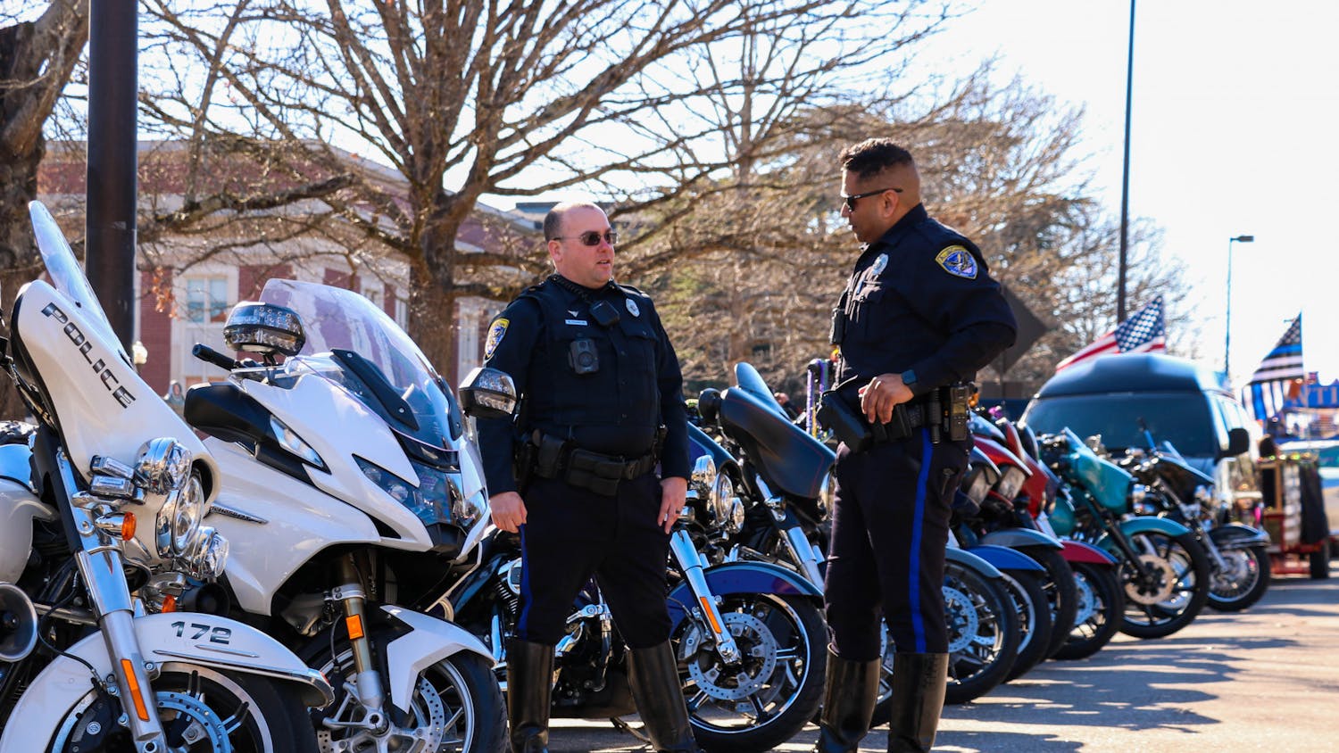 Two officers with the Auburn Police Department chat in front of a row of motorcycles set to lead Auburn's Mardi Gras parade held on Feb. 18, 2023.