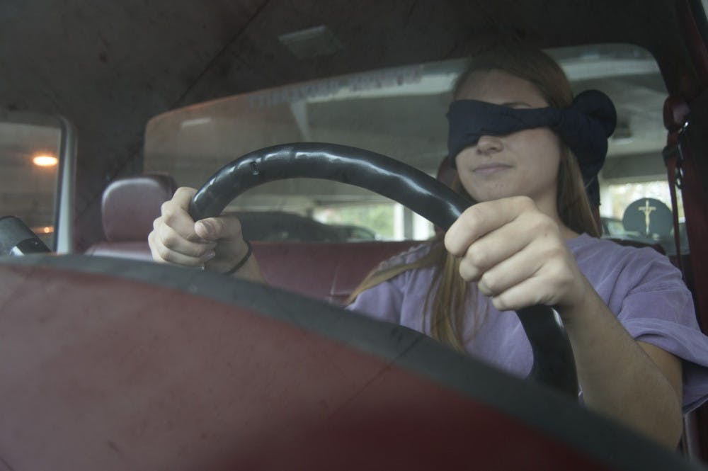 A driver poses blindfolded in a car.&nbsp;