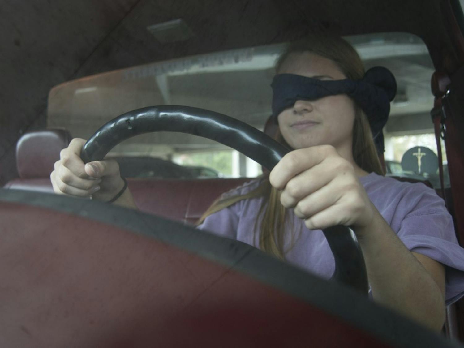 A driver poses blindfolded in a car.&nbsp;