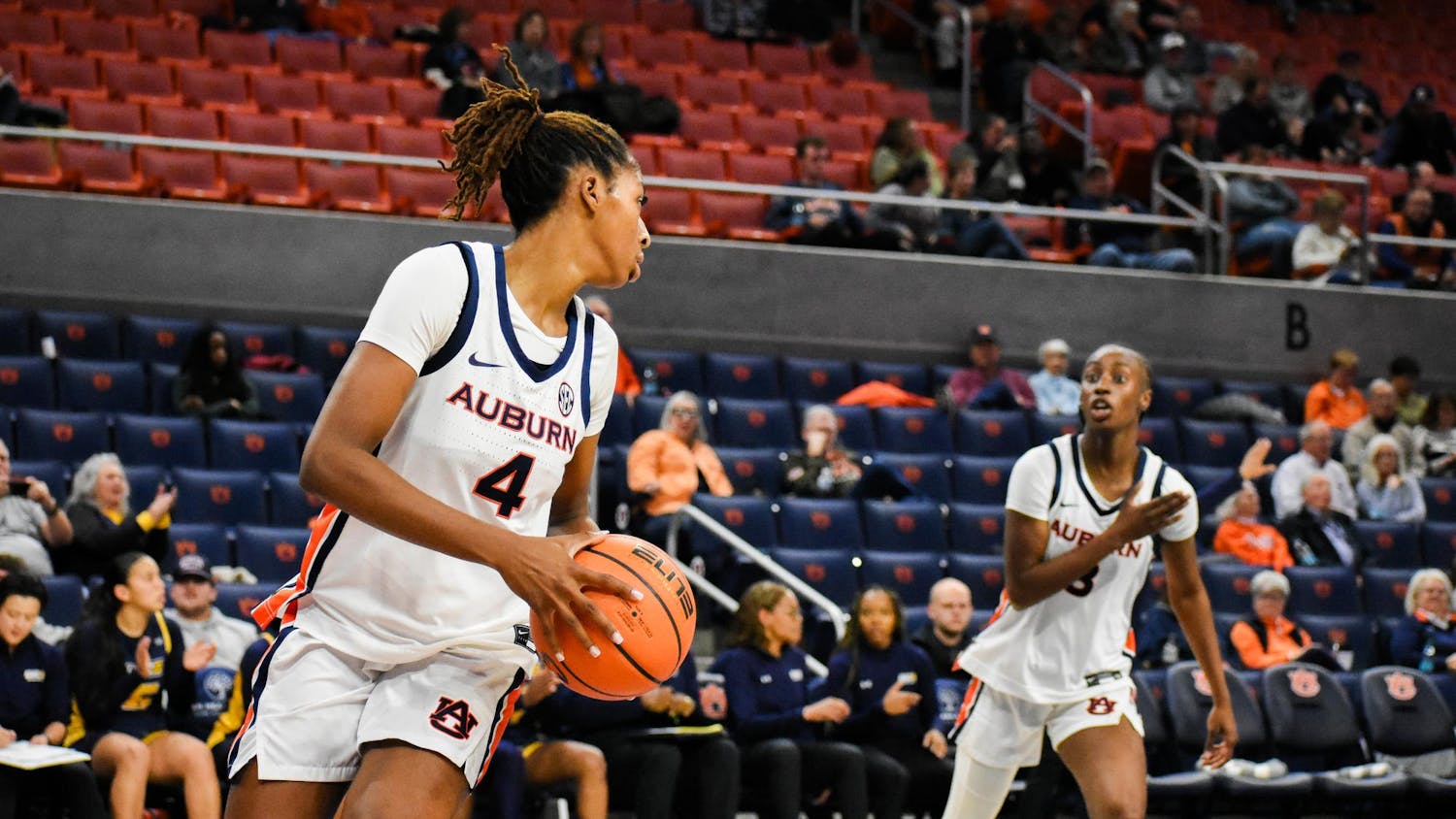 A basketball player in an Auburn uniform prepares to pass the ball while another teammate calls for it nearby, with spectators in the background.