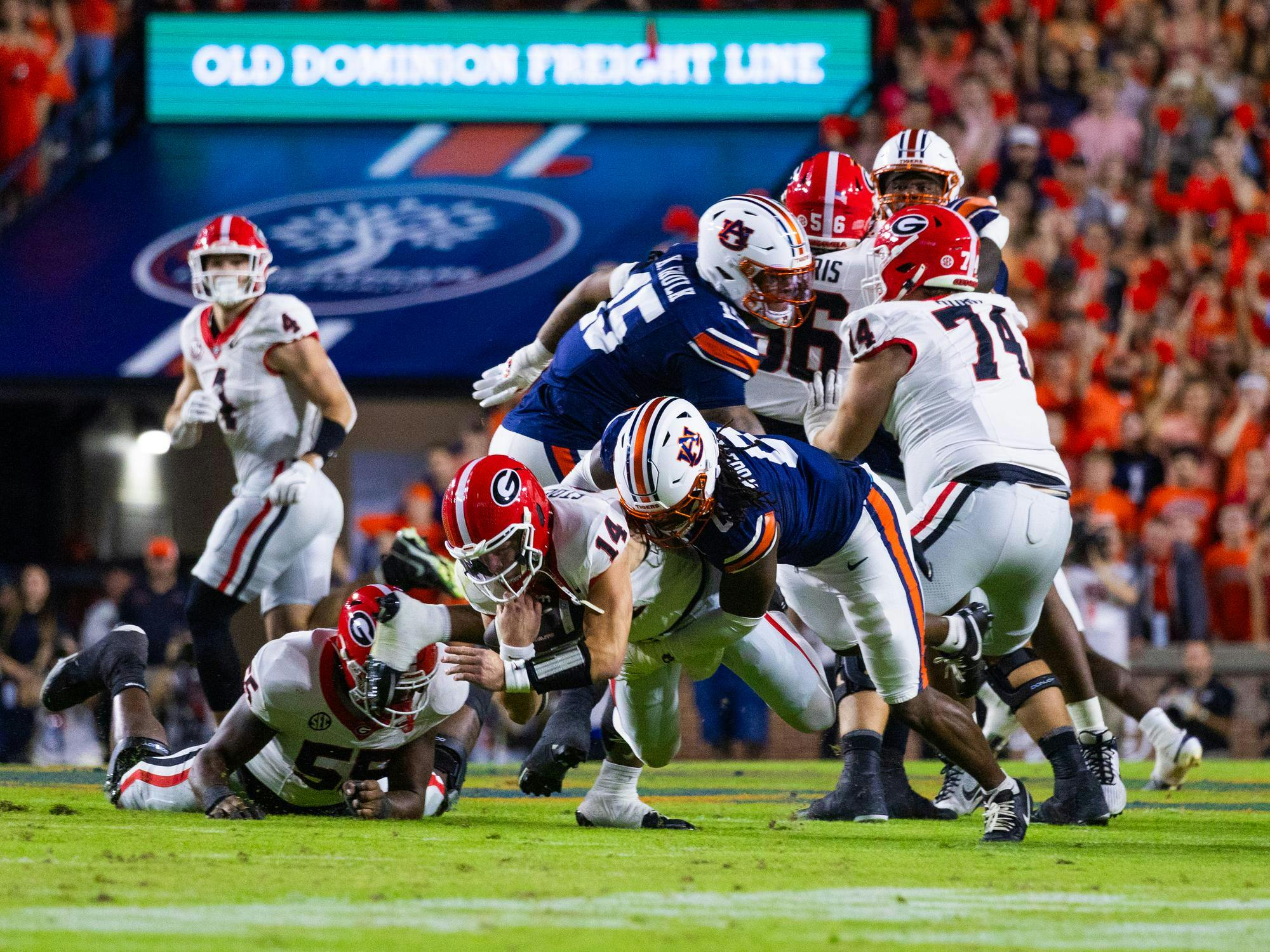 A football player in a red uniform is being tackled by several opponents in a crowded stadium during a game.