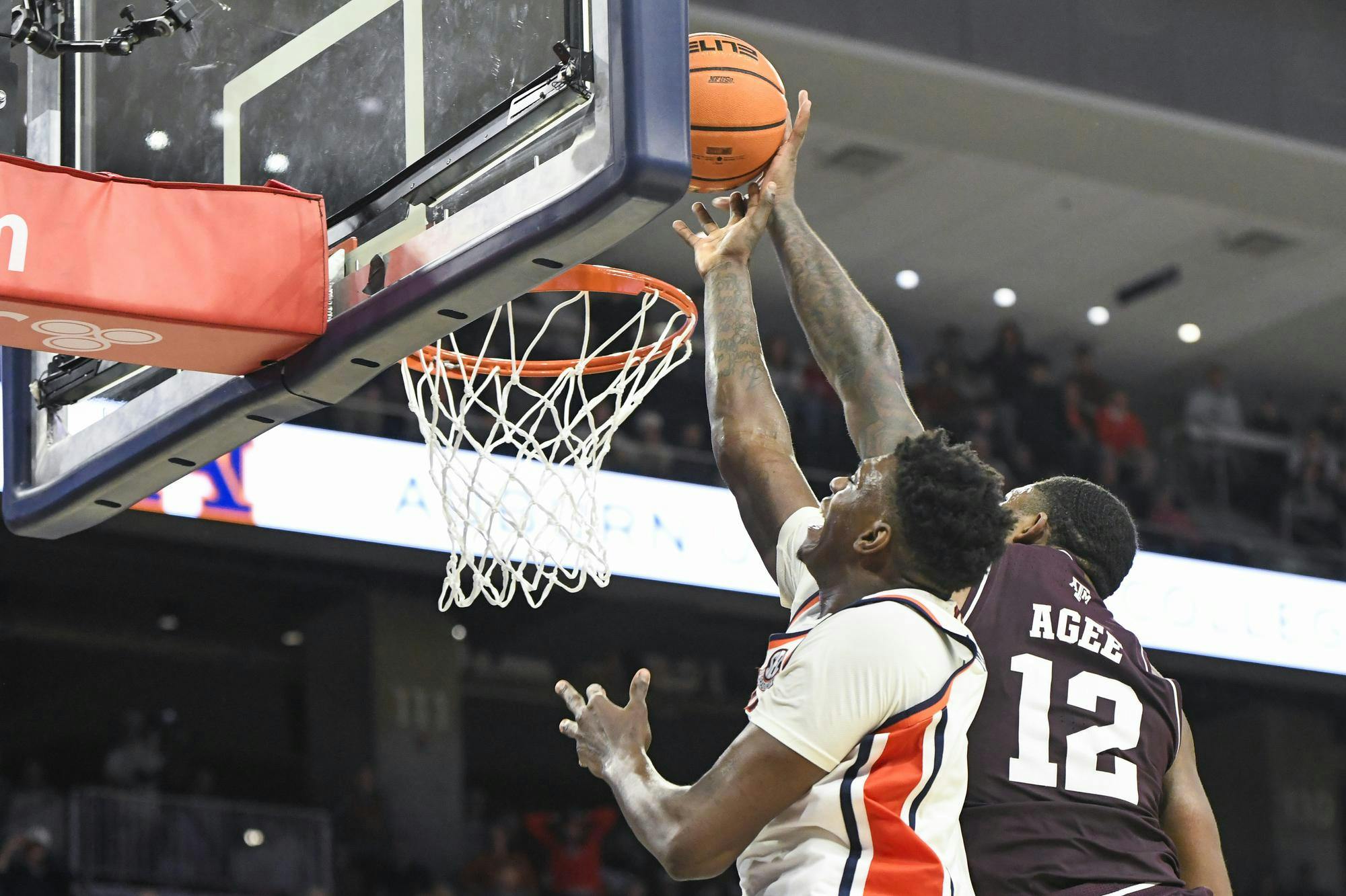 A player jumps towards a basketball hoop, attempting to block another player who is shooting a basketball.