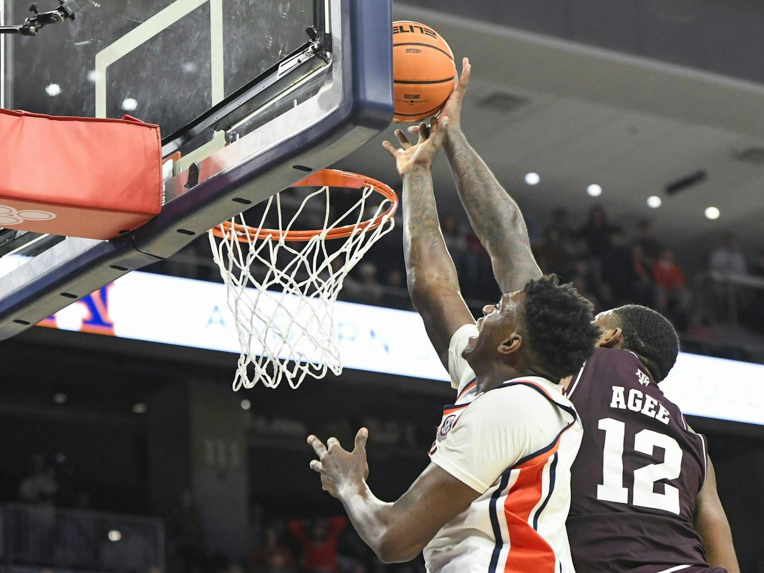 A player jumps towards a basketball hoop, attempting to block another player who is shooting a basketball.