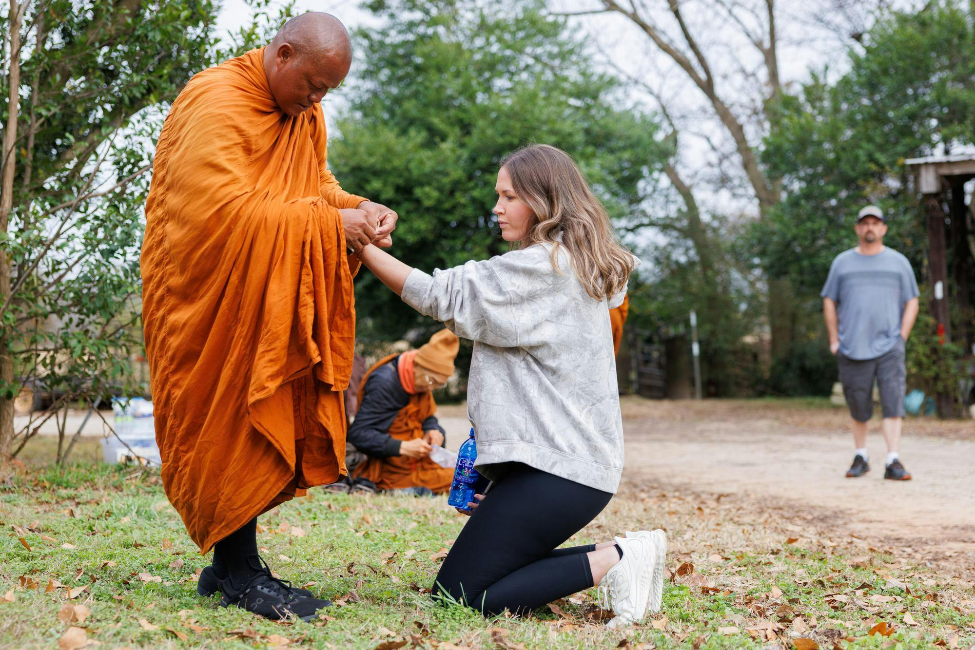A woman shows respect to the Venerable Monk by sitting on her knees and offering up her wrist. The monk then ties a blessing bracelet made from yarn around her wrist.