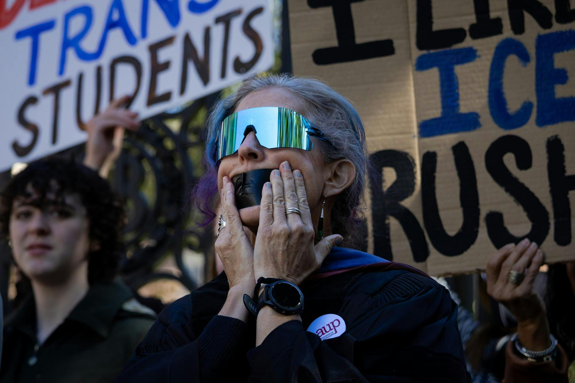Photo of a woman wearing sunglasses applying tape to her mouth.