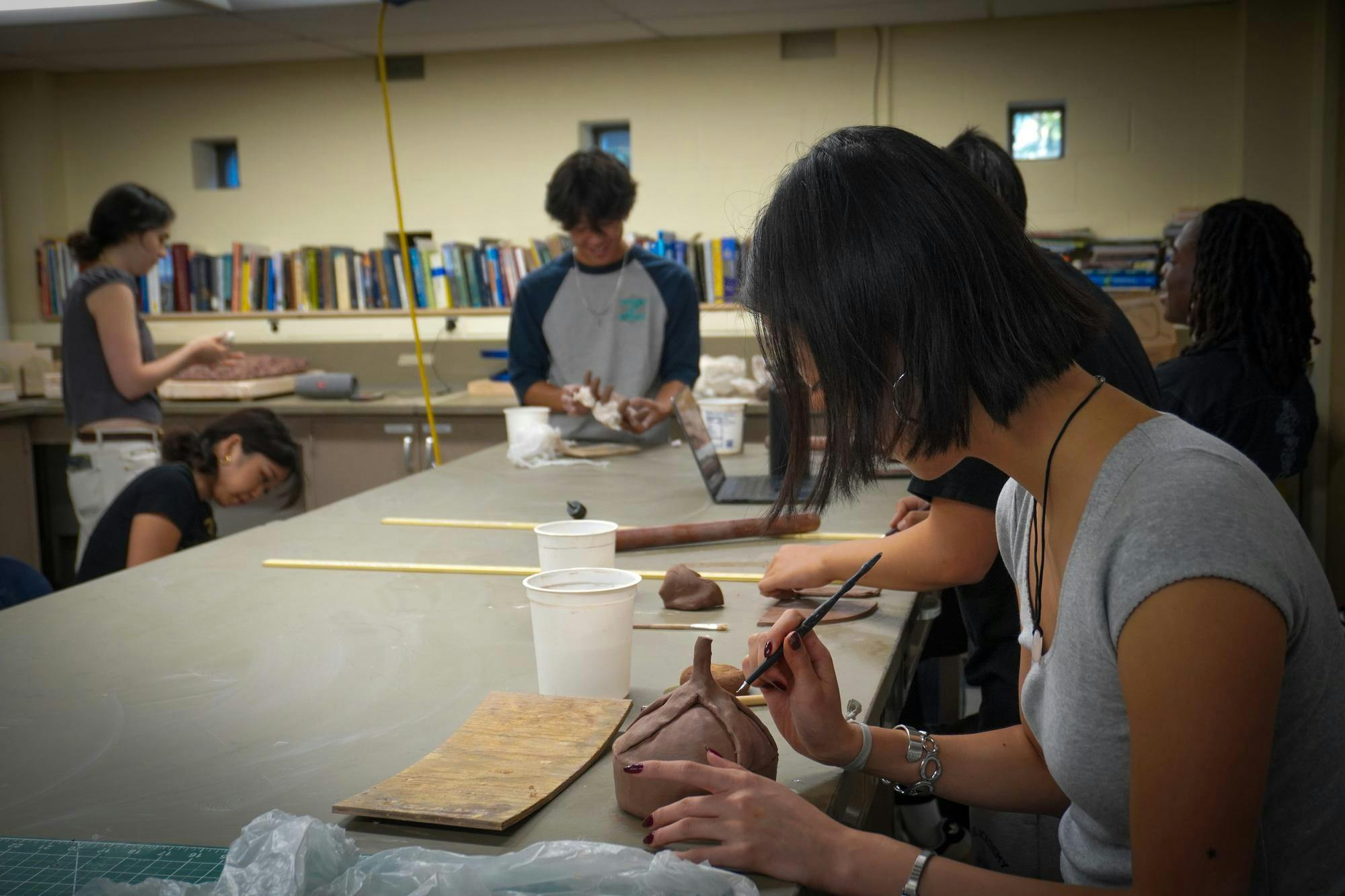 Photo of a student using a pointed tool to sculpt a red, clay pottery piece.