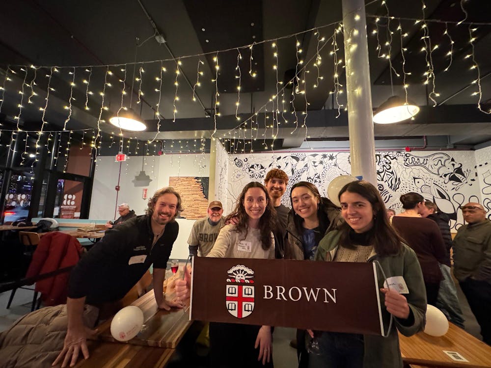Brown students and alums pose with Brown University banner. 
