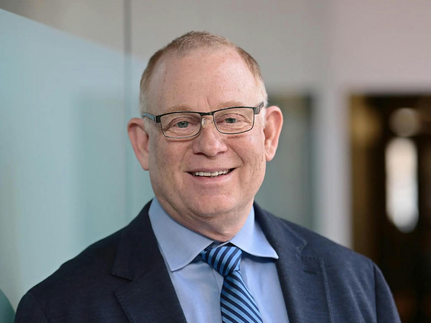 Up close portrait shot of Michael Satlow, who wears glasses and a blue suit, smiling against a blurred background.