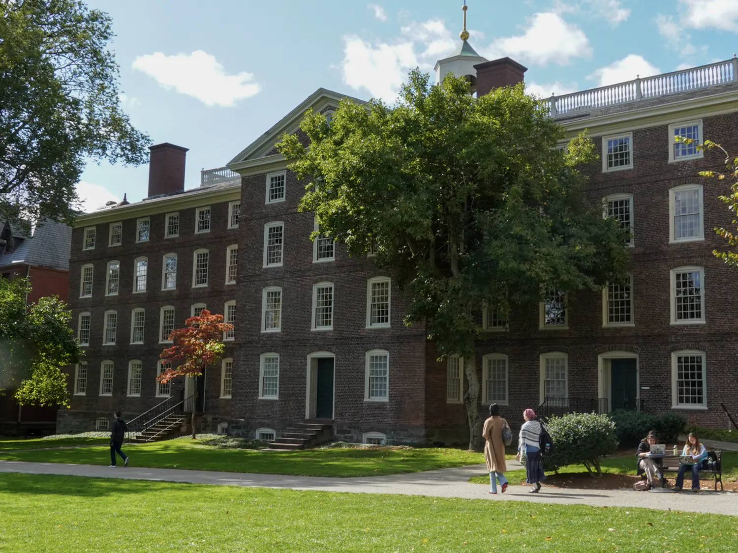 University Hall, a large brick building, sits behind a patch of green grass on a sunny day.