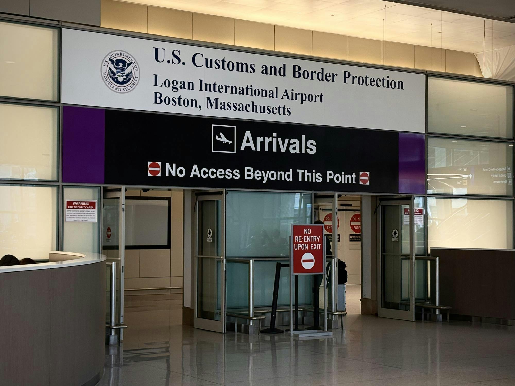 A photo of U.S. Customs and Border Protection at Boston Logan International Airport. A sign reads "Arrivals" and "No Access Beyond This Point." 
