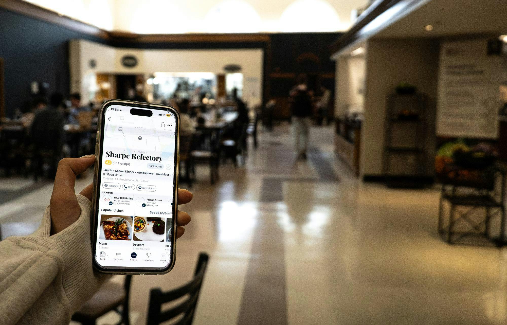 A photo of the Sharpe Refectory with someone’s hand holding a phone, which has the on Beli app open to the “Sharpe Refectory” page.