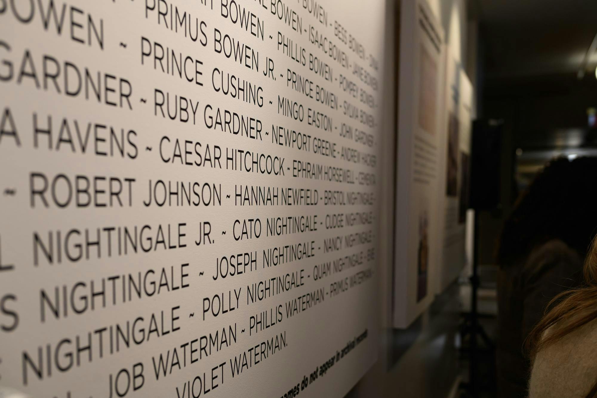 A photo showing a close-up of a vertical panel with names listed as visitors walk past. 