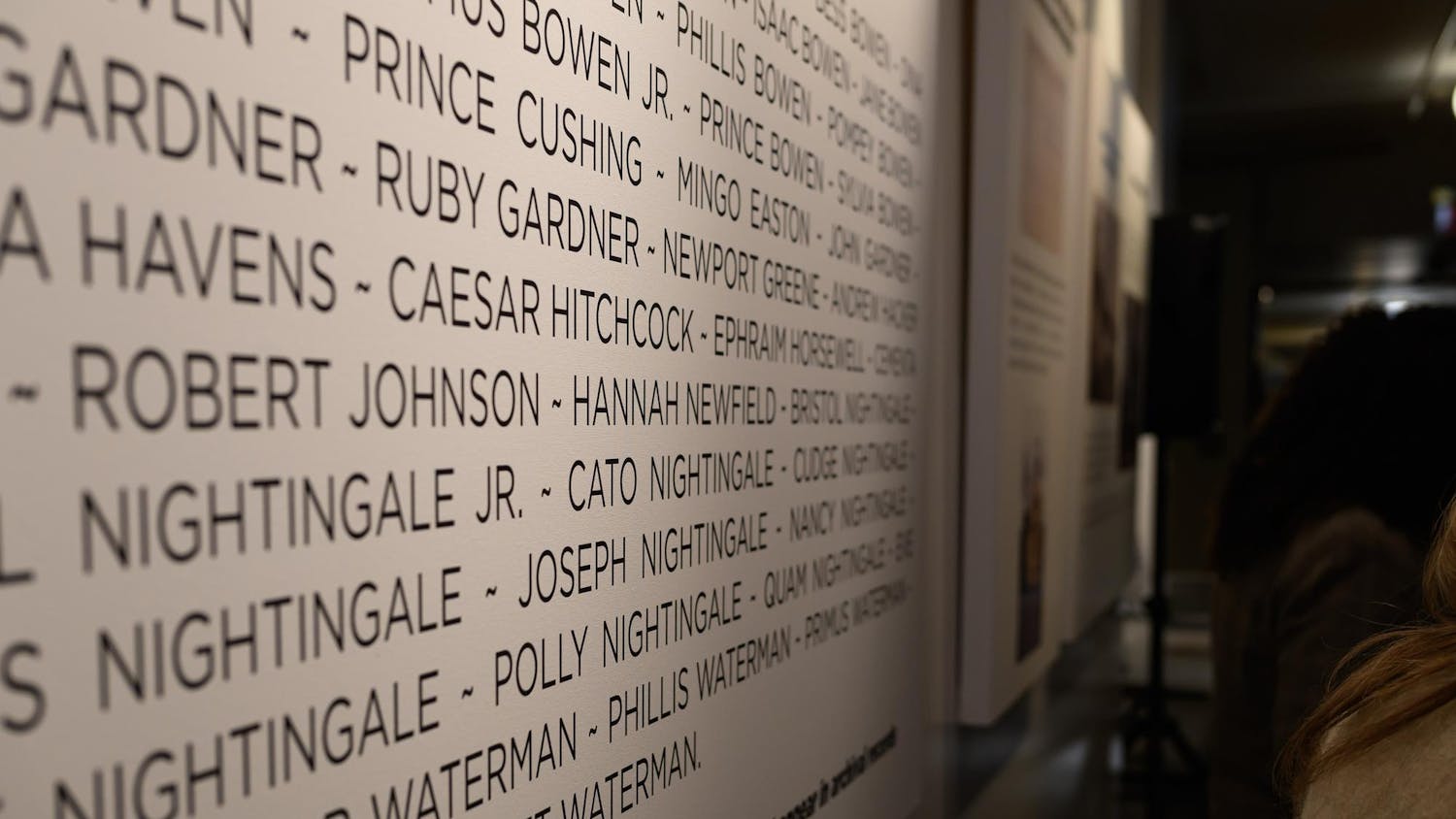 A photo showing a close-up of a vertical panel with names listed as visitors walk past.