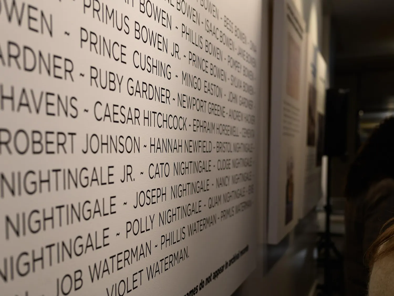 A photo showing a close-up of a vertical panel with names listed as visitors walk past.