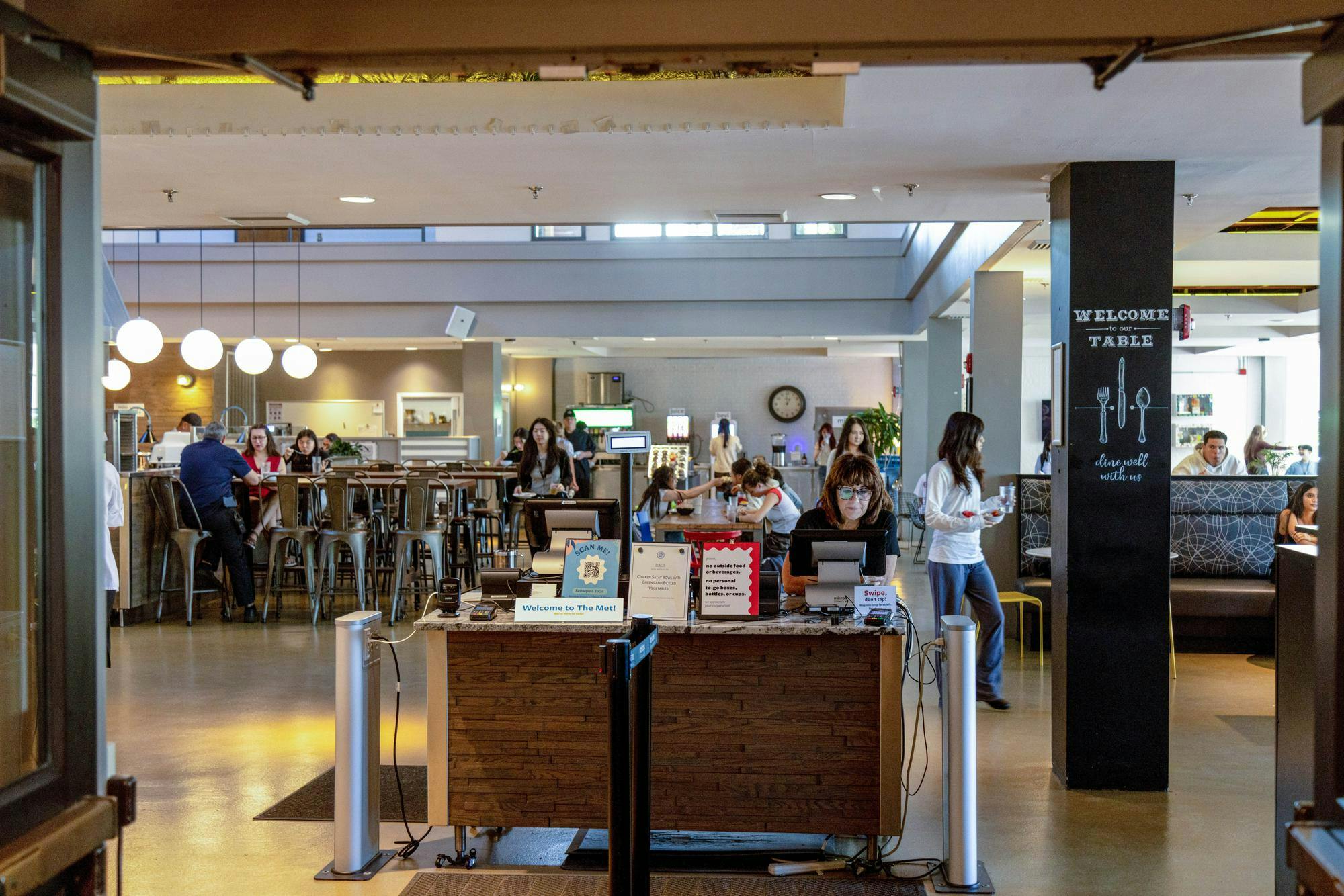 A photo depicts the RISD dining hall through its entrance doors. A woman in glasses sits at the check-in table. 

