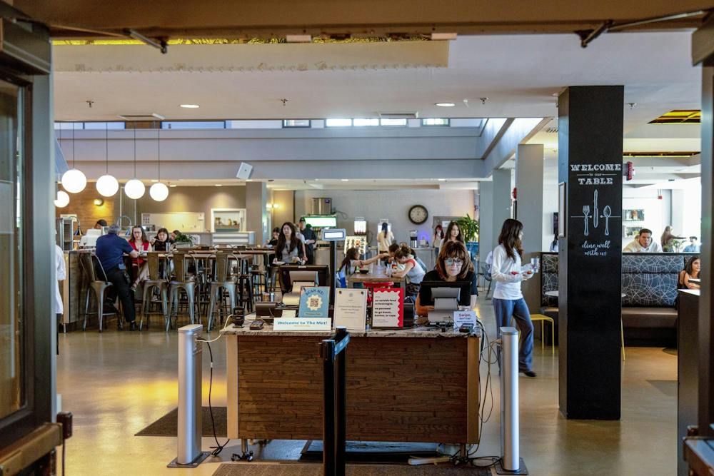 A photo depicts the RISD dining hall through its entrance doors. A woman in glasses sits at the check-in table. 

