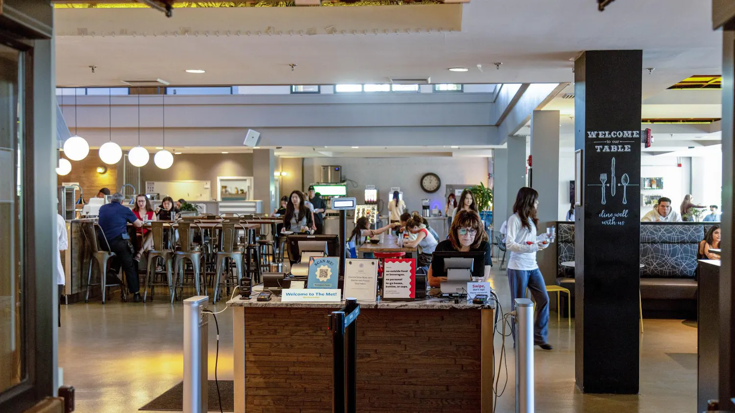 A photo depicts the RISD dining hall through its entrance doors. A woman in glasses sits at the check-in table.