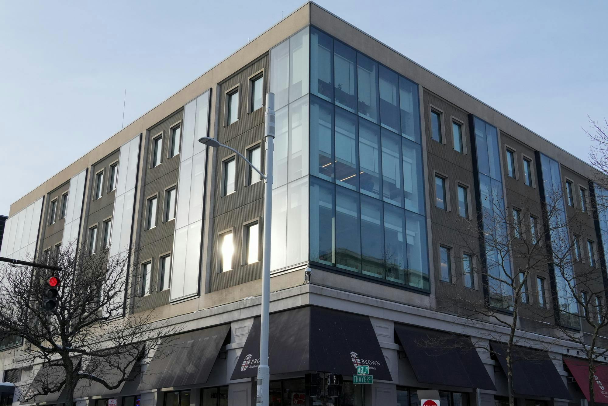 Photo of the corner side of a building filled with a window reflecting light and a light post in front of it.