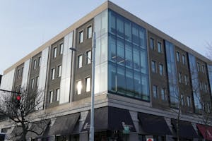 Photo of the corner side of a building filled with a window reflecting light and a light post in front of it.