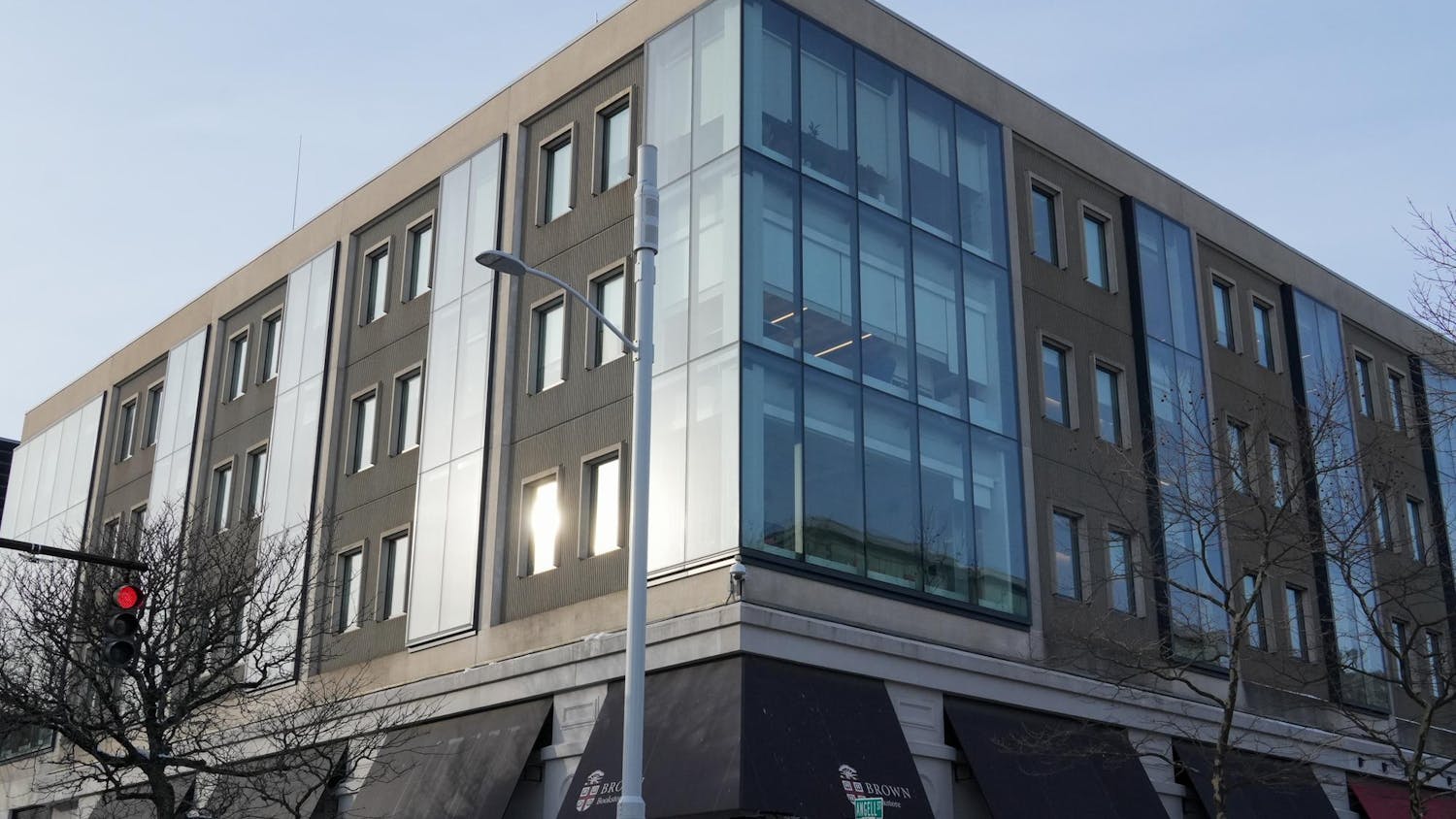 Photo of the corner side of a building filled with a window reflecting light and a light post in front of it.