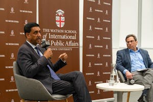 Ro Khanna, in a grey suit, sits in a chair next to moderator Eric Patashnik, director of the Taubman Center. The two are in front of a brown backdrop. 