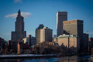 Photograph of buildings in downtown providence with a sliver of the river visible in the bottom of the photo and blue skies above the buildings.