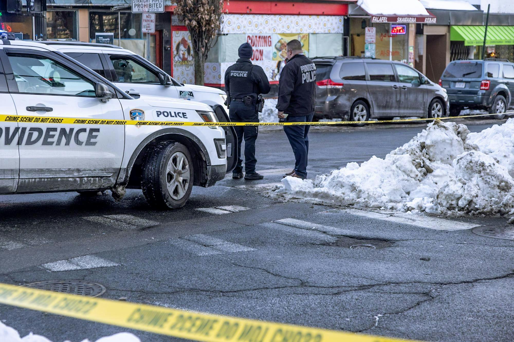 A photograph of two Providence Police officers standing in front of yellow caution tape and a parked police car.