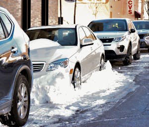 Photo of a white sedan surrounded by a pile of snow parked on the side of the road.