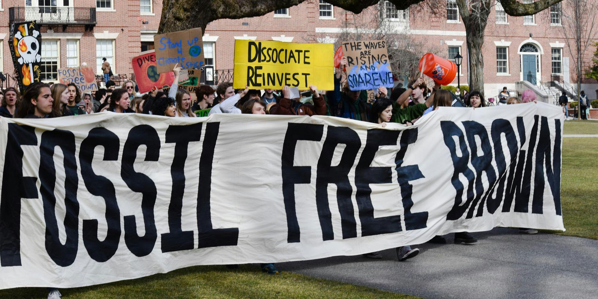 Students protest on the main green holding a large sign reading "Fossil Free Brown." 