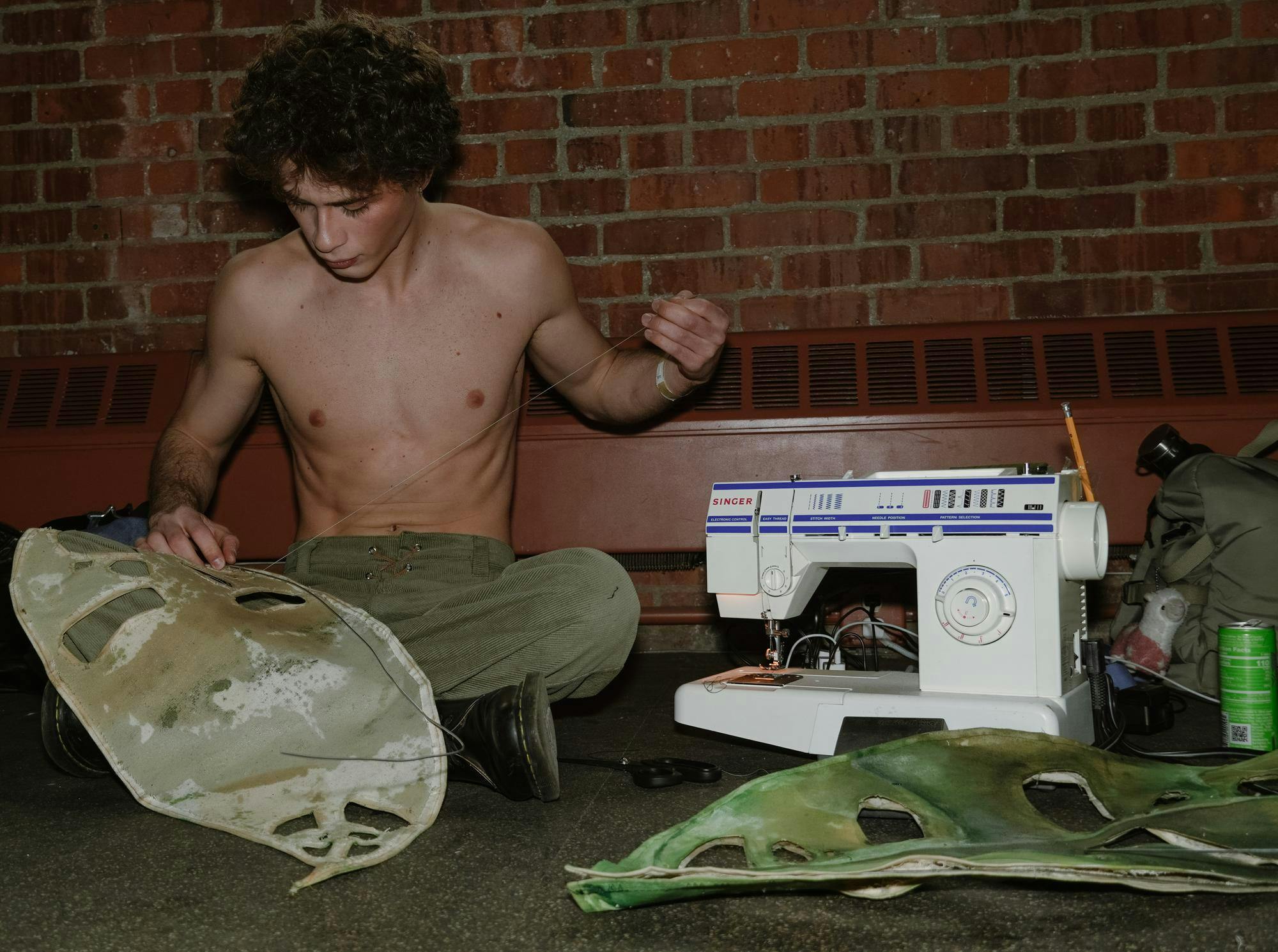 Photo of a designer sitting on the floor with a sewing machine hand sewing part of an outfit.