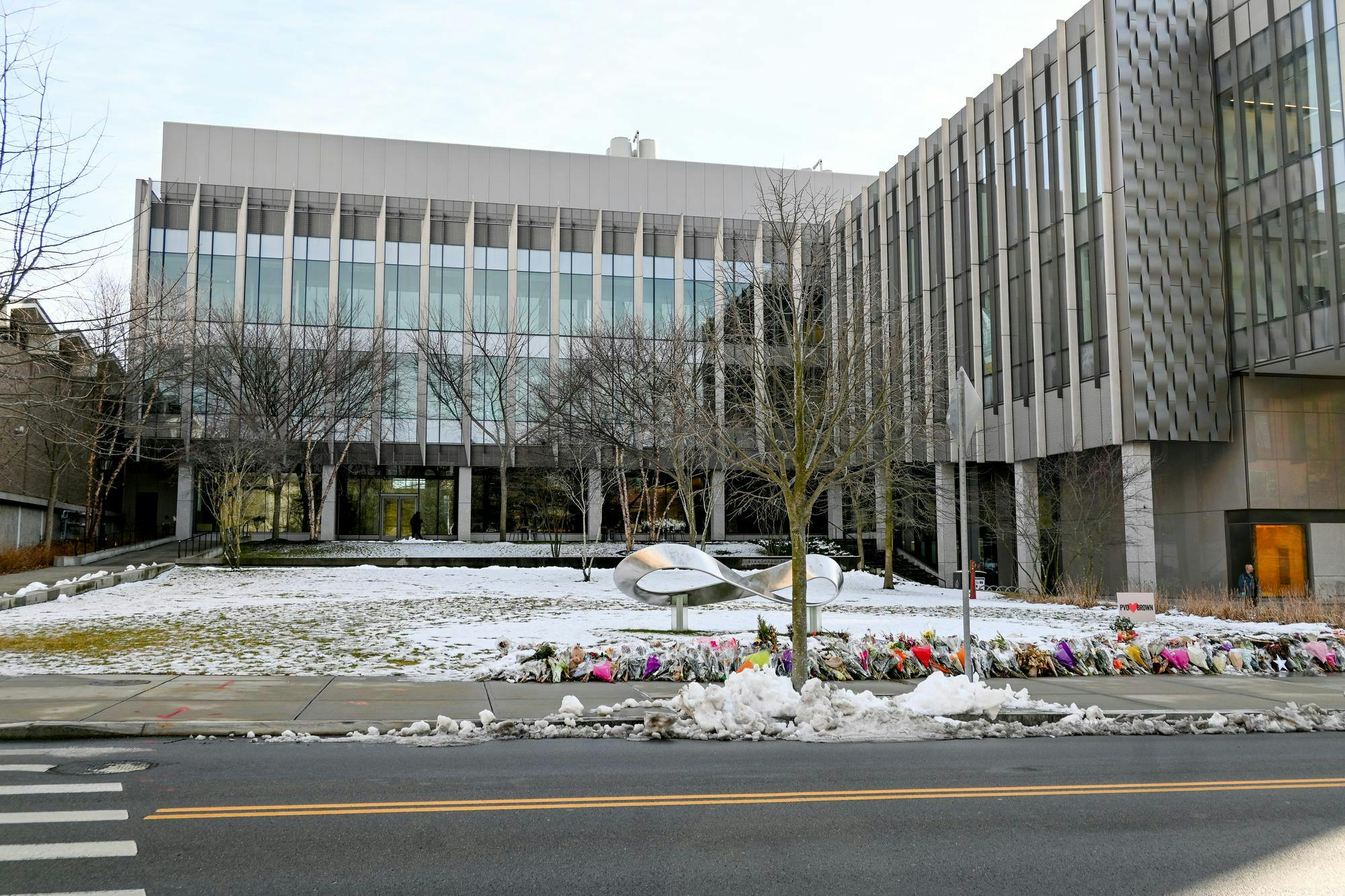 An outside shot of snowy Barus and Holley with flowers lining the street as part of the memorial for Ella Cook '28 and Mukhammad Aziz Umurzokov '29