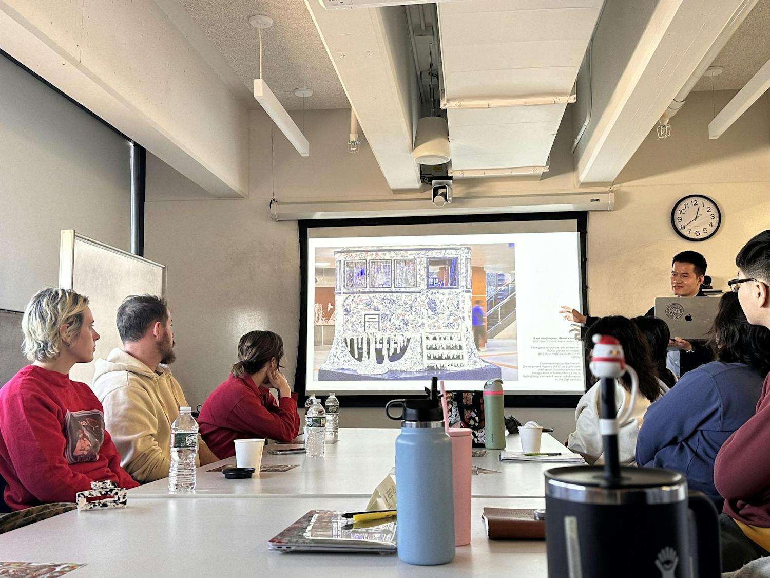 Xuân-Lam Nguyễn stands in front of a screen displaying his artwork to participating viewers.