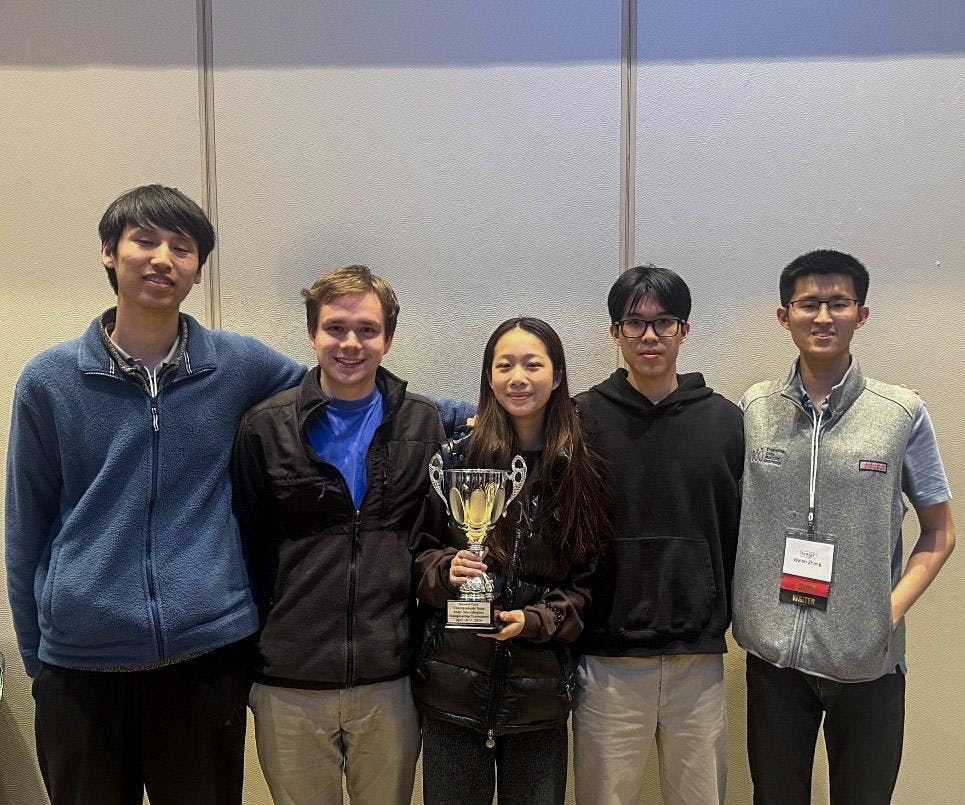 A photo of five students with the middle individual holding a trophy. 