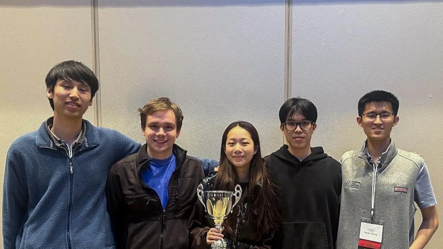 A photo of five students with the middle individual holding a trophy.