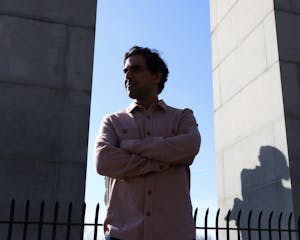 A photo of Mahajan crossing him arms, with two pillars to the side of him, and a shadow casting over his face.