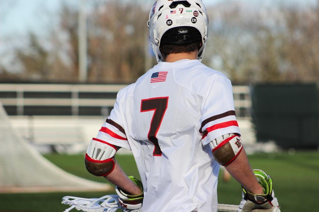 Photo of a Brown men's lacrosse player on the field from behind.