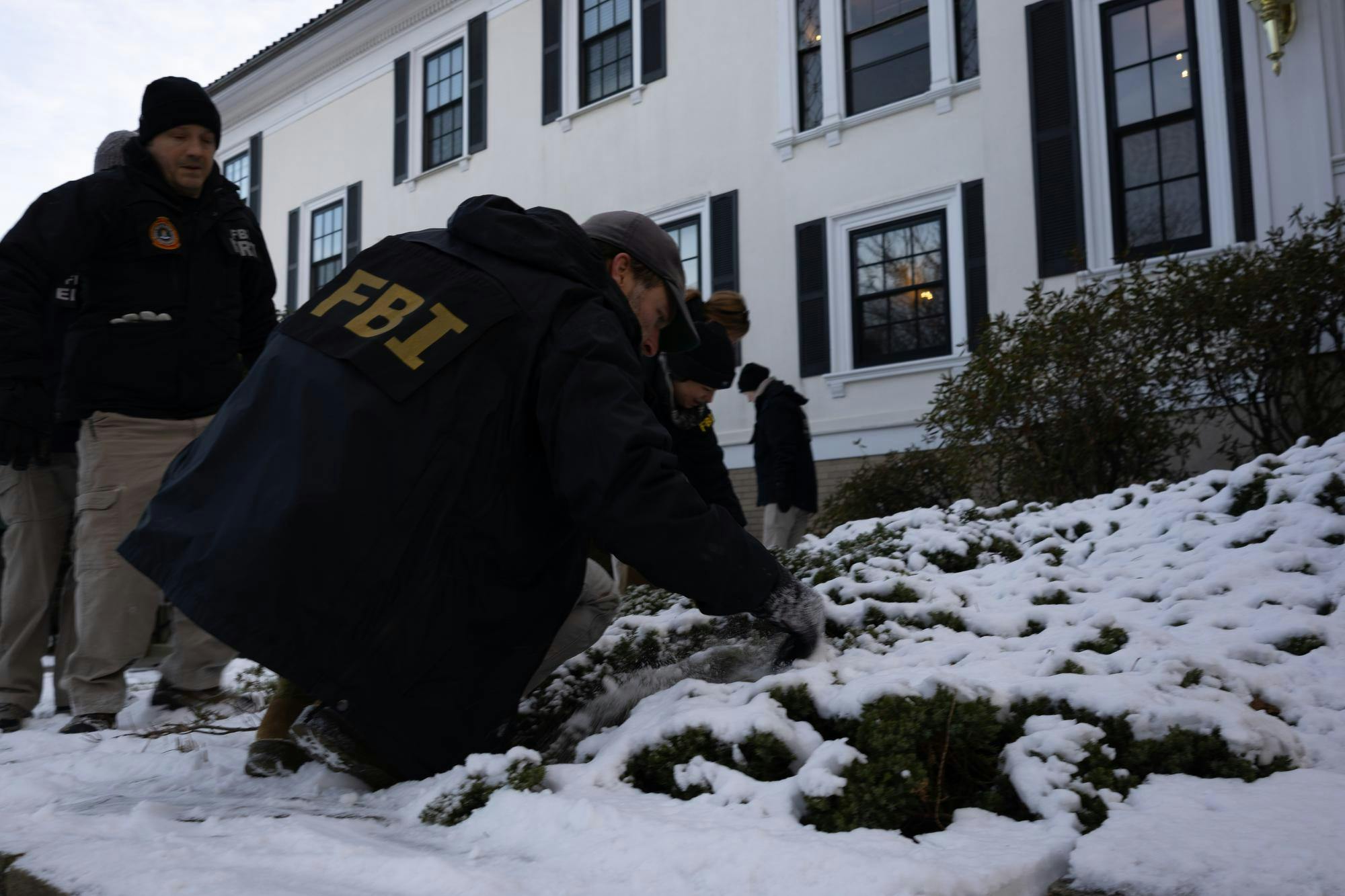 FBI agents dig through snowy bushes. 