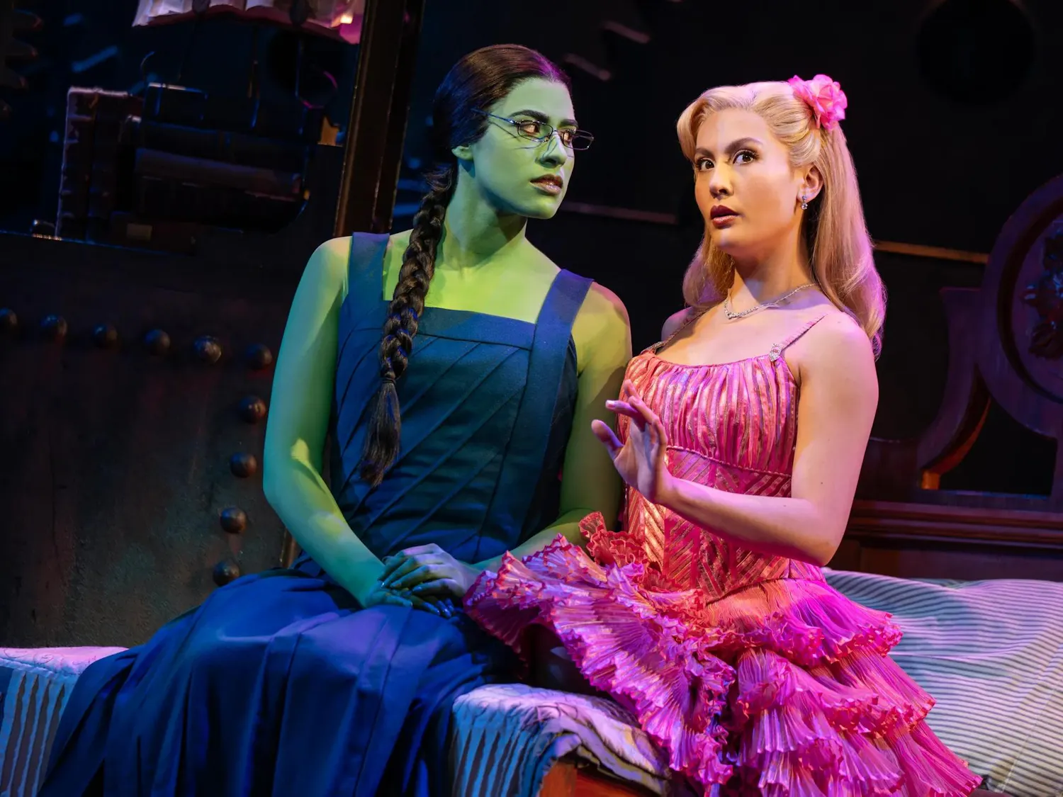 A photo of the musical shows two actresses, one in green body paint, the other in a pink dress.