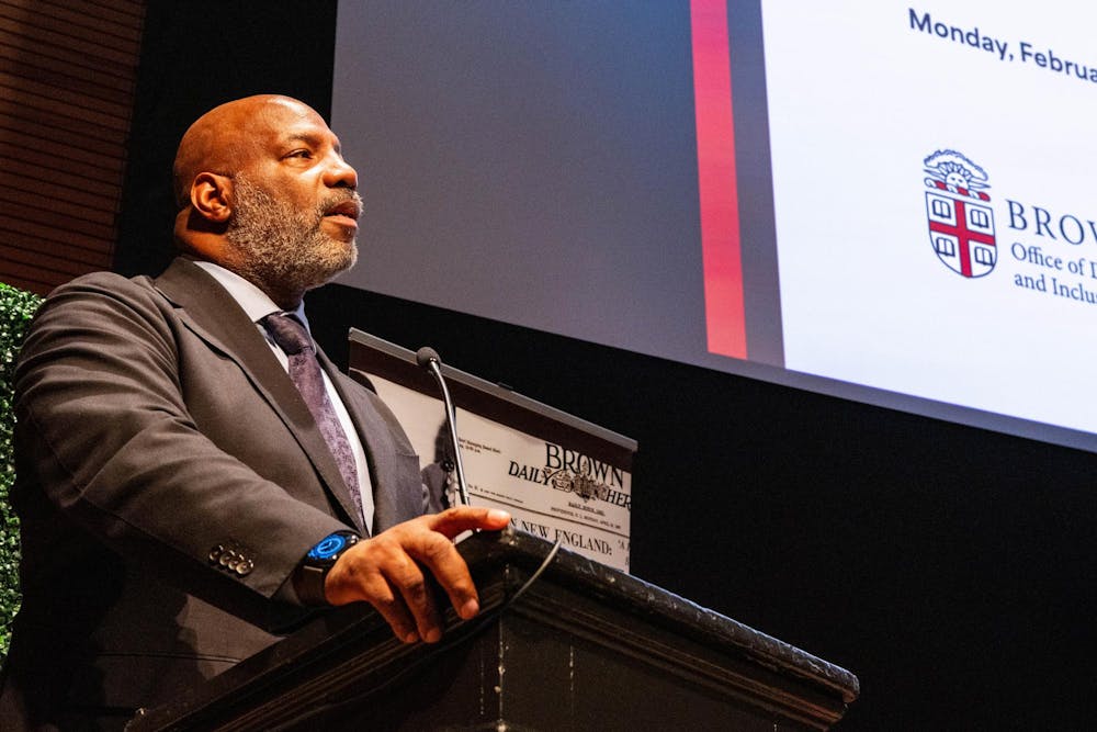 A man in a suit standing at a lectern with his mouth slightly open.