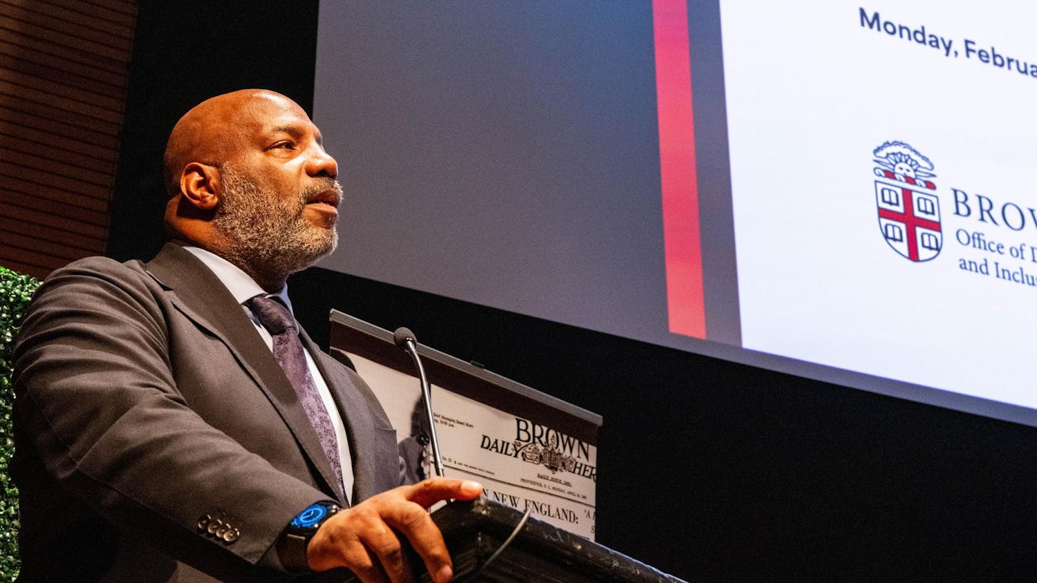 A man in a suit standing at a lectern with his mouth slightly open.