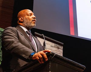 A man in a suit standing at a lectern with his mouth slightly open.