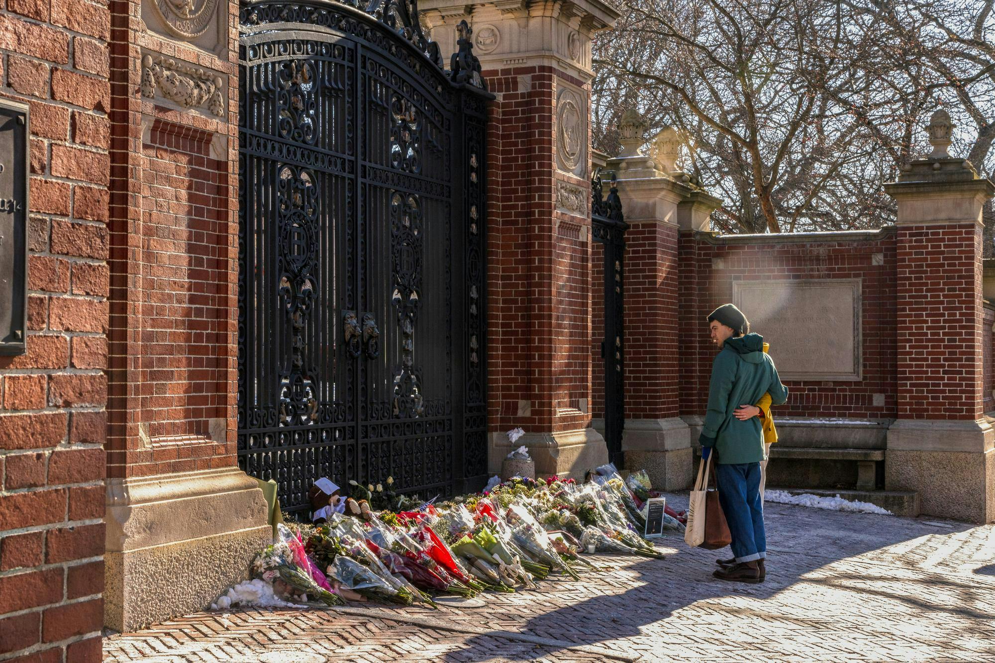 Photo of two individuals standing embracing each other from the side as they look at bouquets of flowers in front of the Van Wickle Gates.