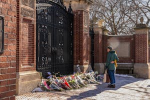 Photo of two individuals standing embracing each other from the side as they look at bouquets of flowers in front of the Van Wickle Gates.