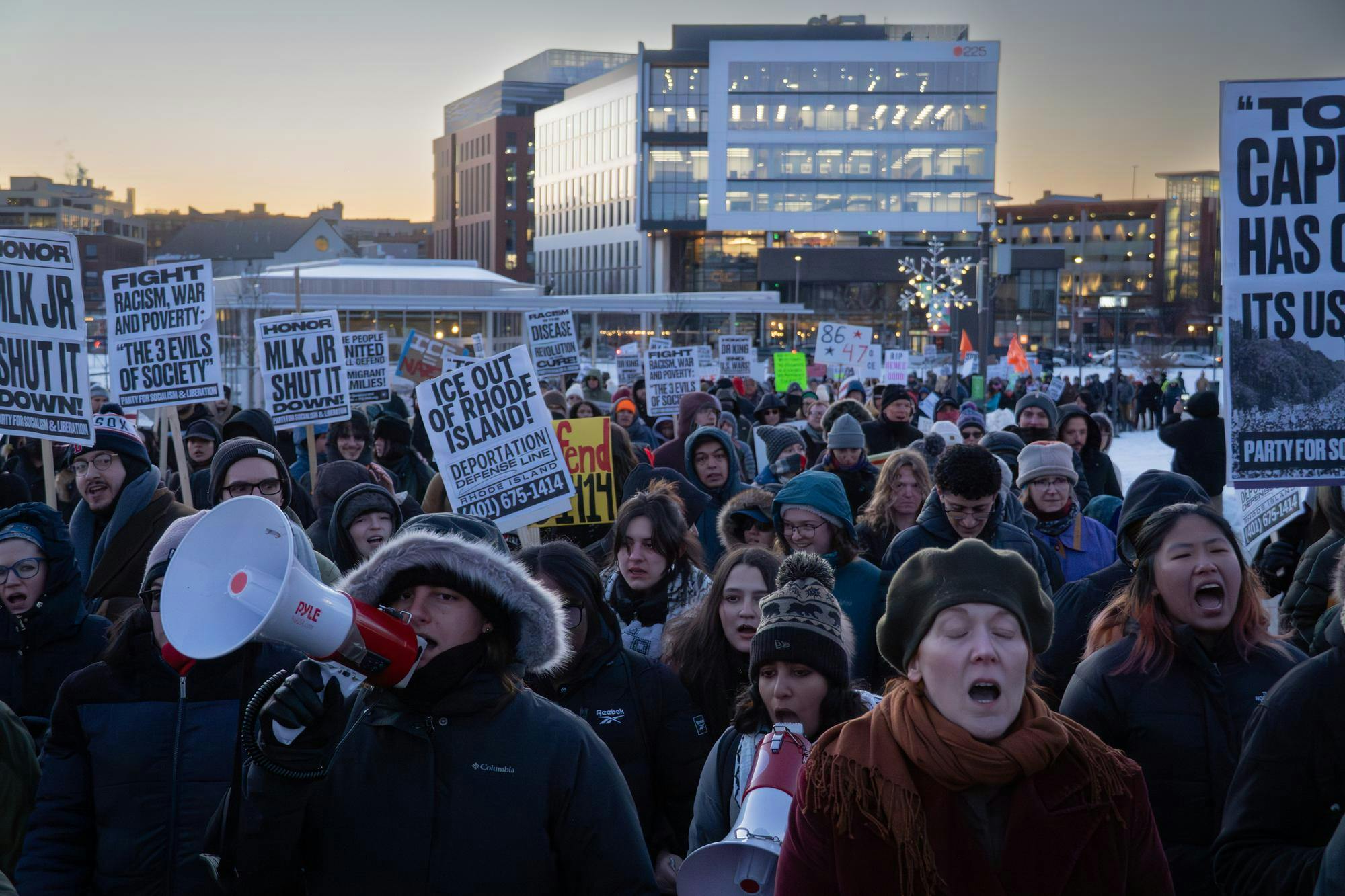 Protestors marching. Many hold different signs, and some hold megaphones. Many are mid-chant.
