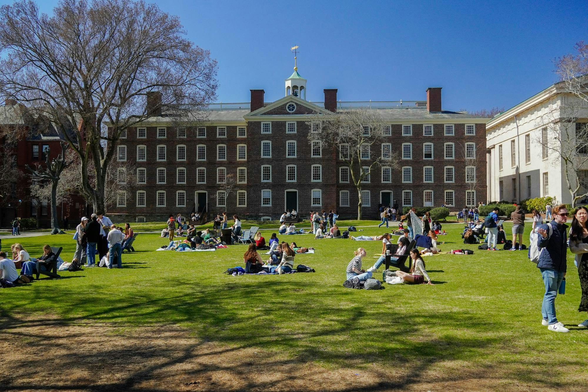 A photo of the Main Green on a sunny day shows students on picnic blankets and University Hall.
