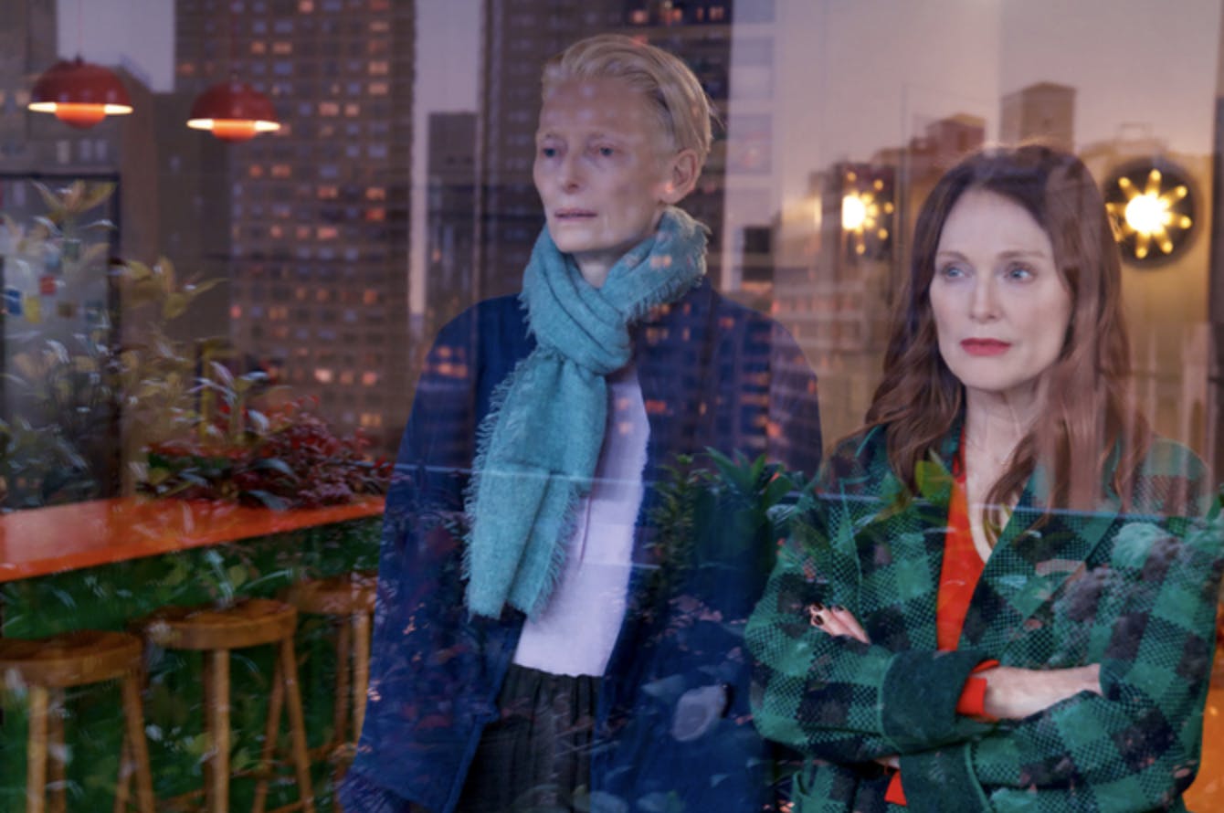 Tilda Swinton and Julianne Moore look out a window at a city skyline.